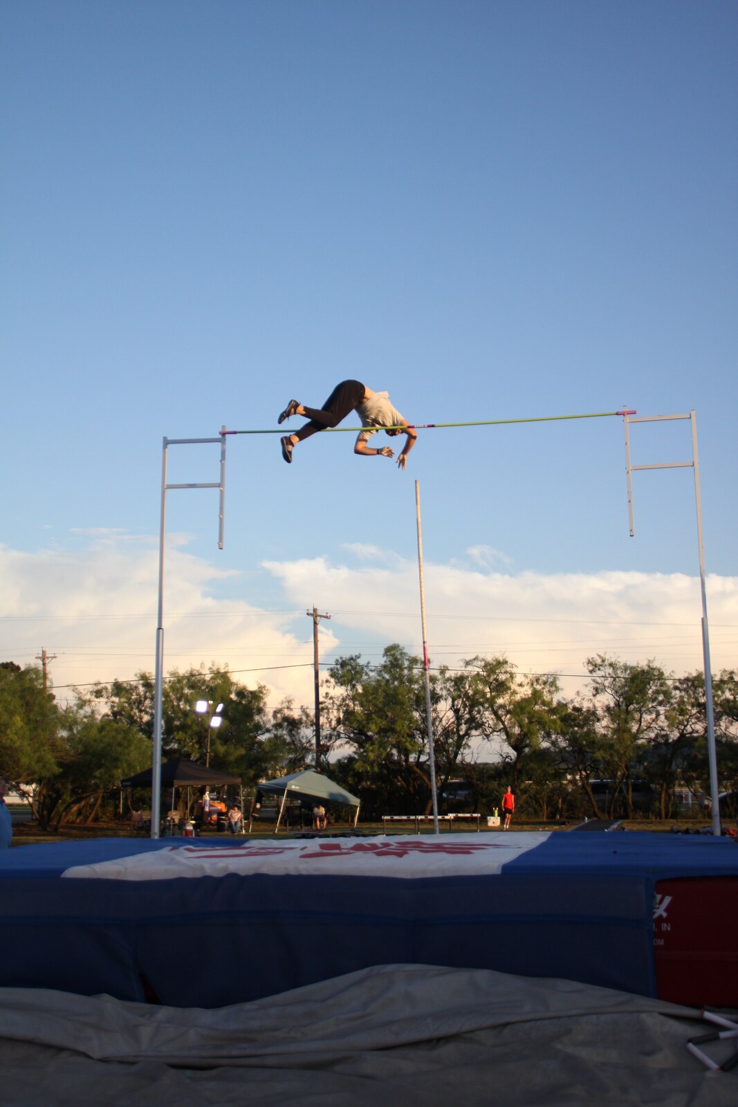 A pole vaulter clearing the crossbar at an outdoor meet.